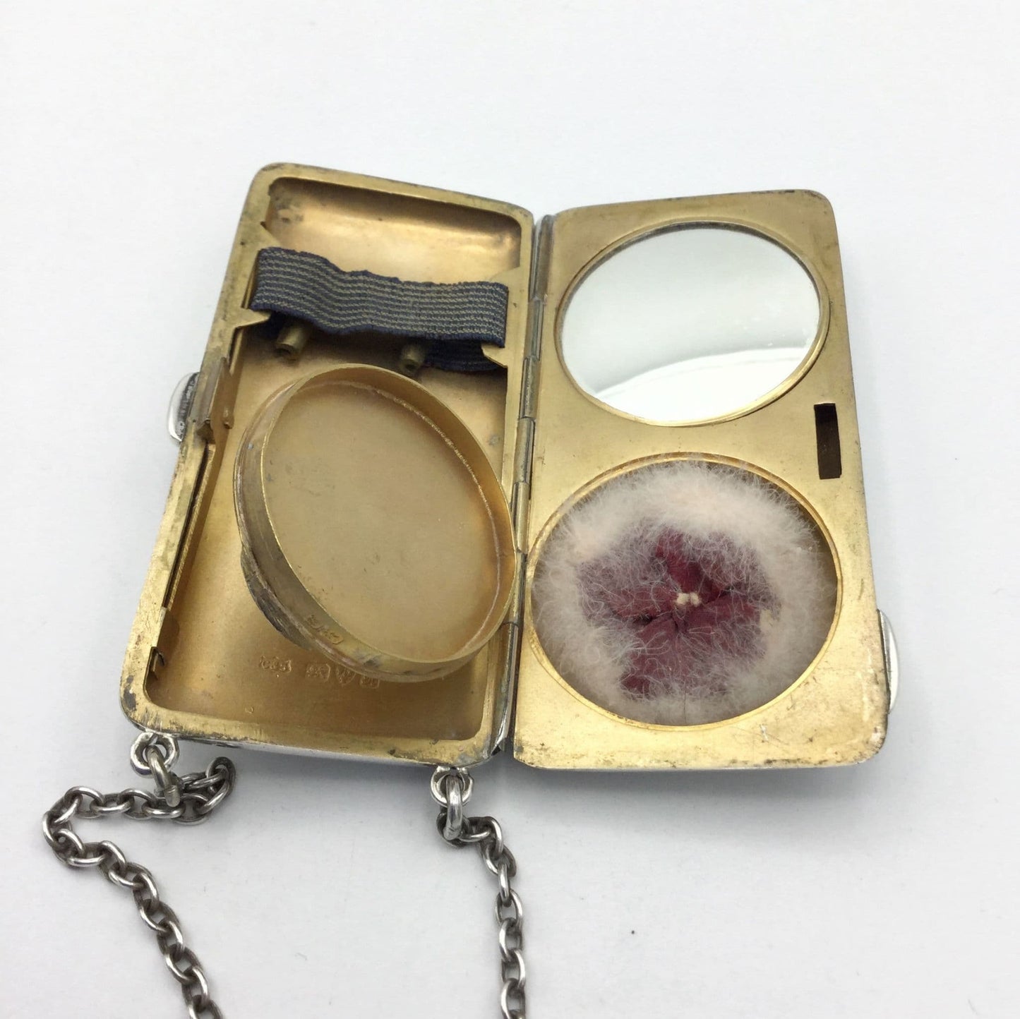 gilded golden inside of case showing a mirror, powder area with an open lid, a powder puff and chain