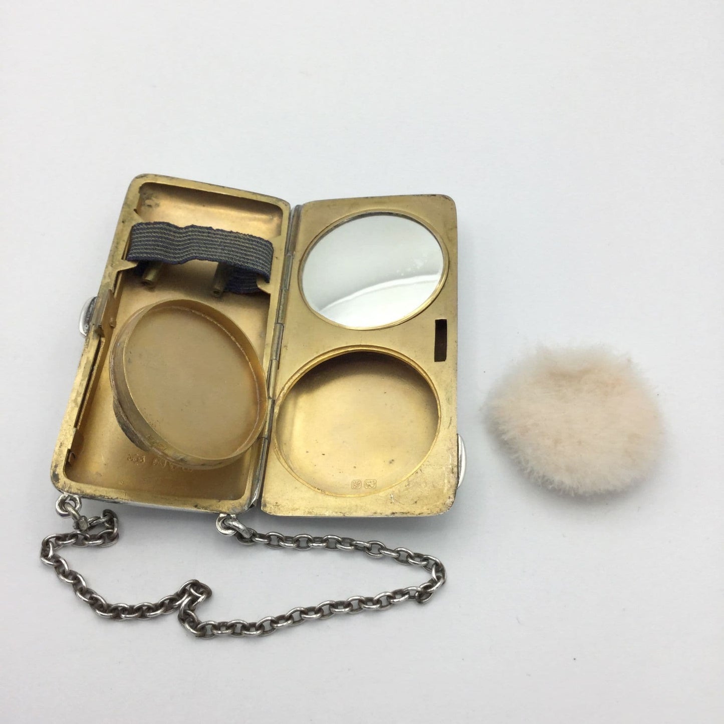gilded golden inside of case showing a mirror, powder area and chain, with the unused powder puff at the side