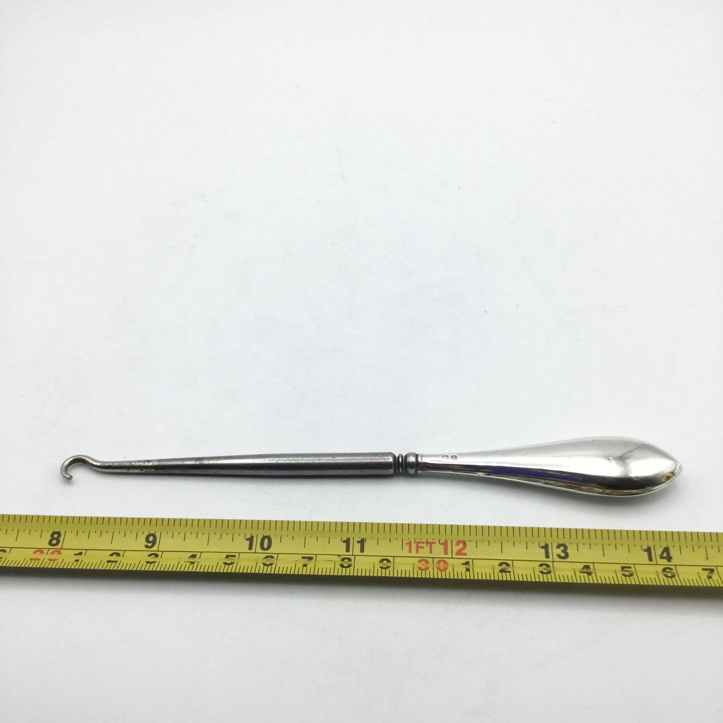 Silver handled button hook with a shiny handle and steel hook next to a tape measure showing the length as 16.5cm