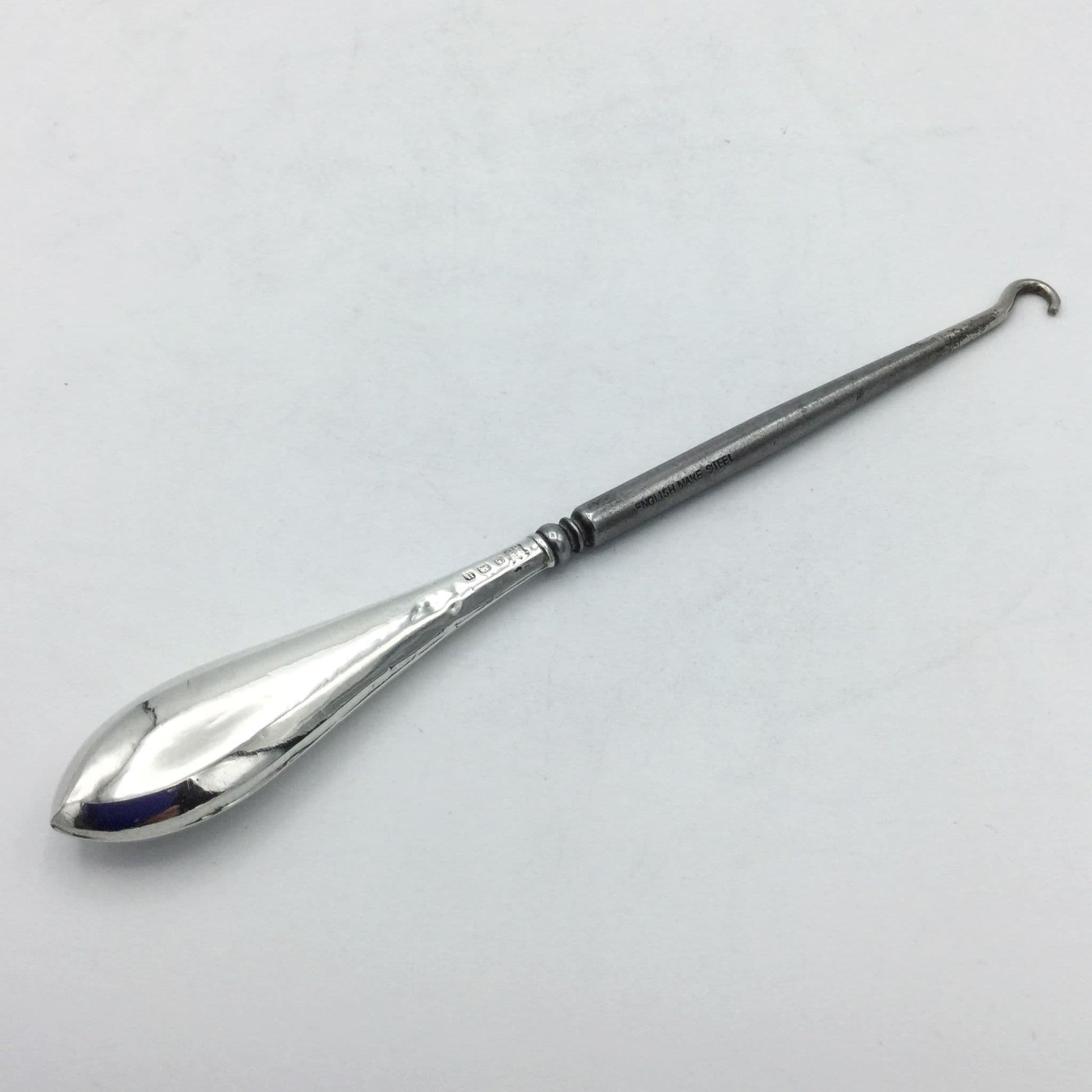Silver handled button hook with a shiny handle and steel hook with hallmarks on a white background