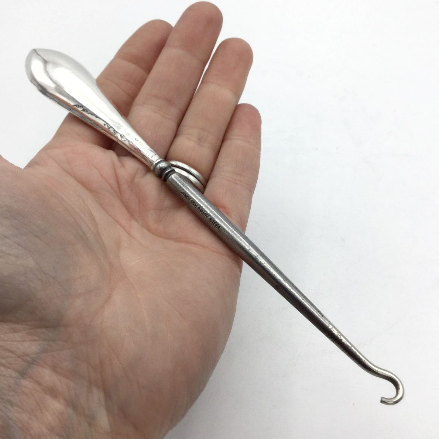 Silver handled button hook with a shiny handle and steel hook held in a hand
