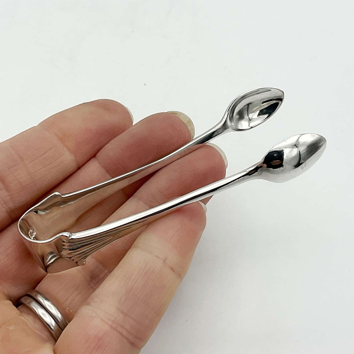 Silver sugar tongs showing an art deco design sitting on fingers