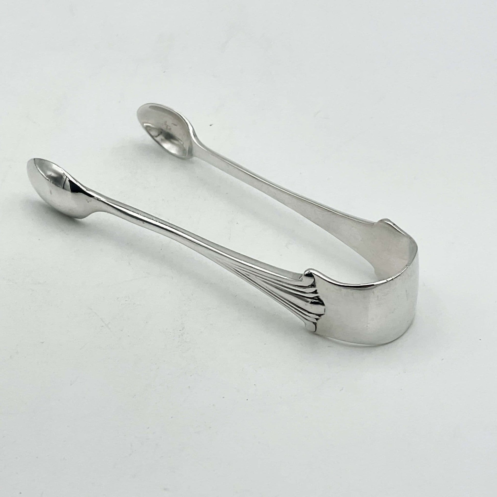 Silver sugar tongs showing an art deco design on a white background