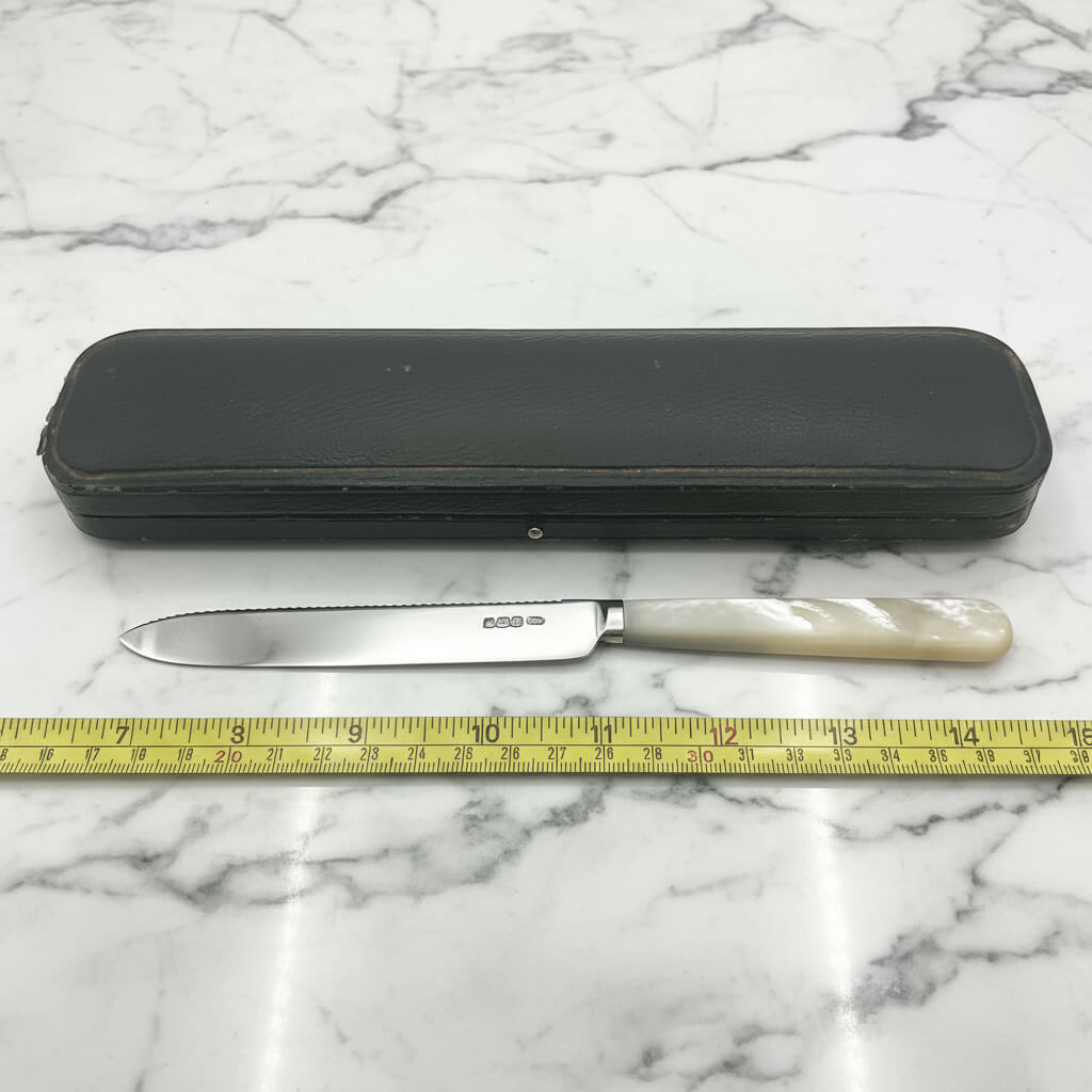 silver knife next to a black presentation box and tape measure on a marble worktop