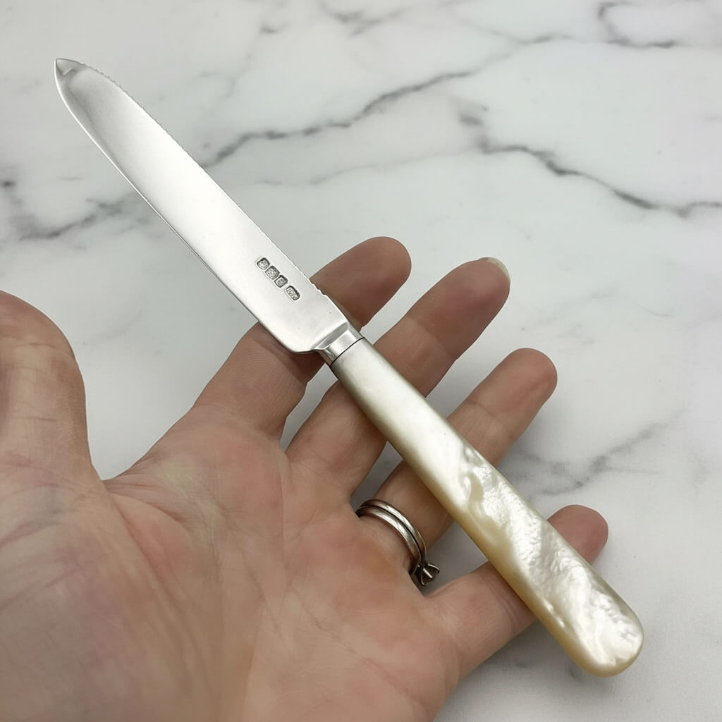 silver knife with mother of pearl handle held in a hand with a marble worktop