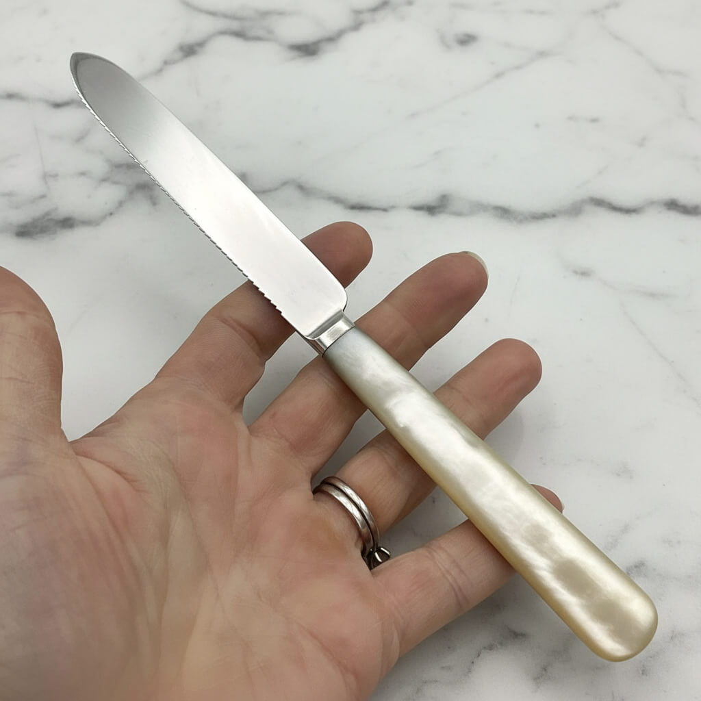 silver knife with mother of pearl handle held in a hand with a marble worktop