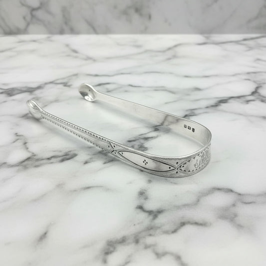 Antique silver sugar tongs on a marble surface
