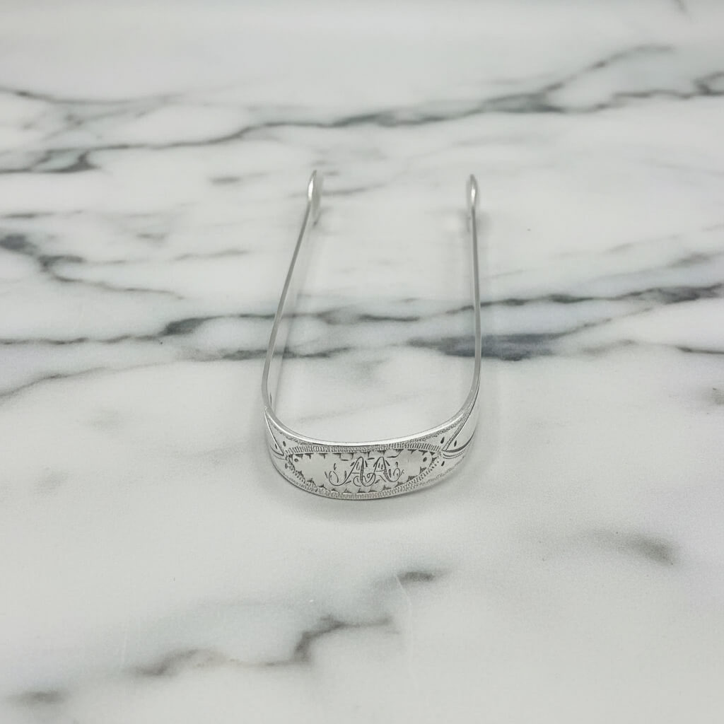 antique silver sugar ongs with AA on the end on a marble surface