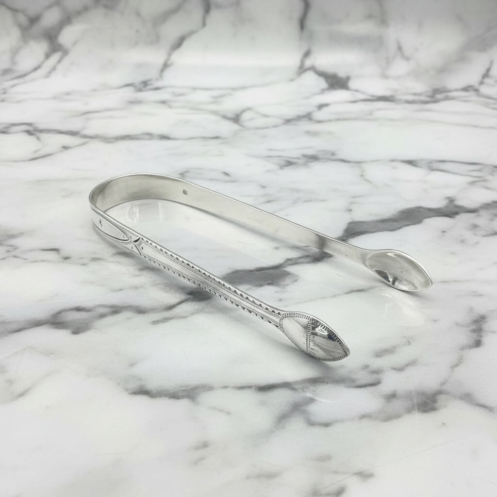 Antique silver sugar tongs on a marble surface