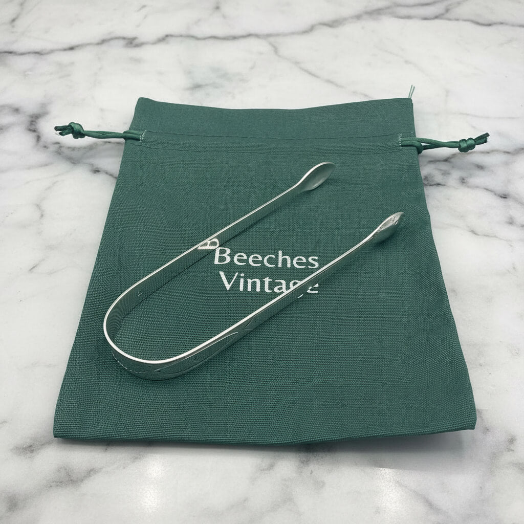 Antique silver sugar tongs on a green Beeches Vintage gift bag on a marble surface