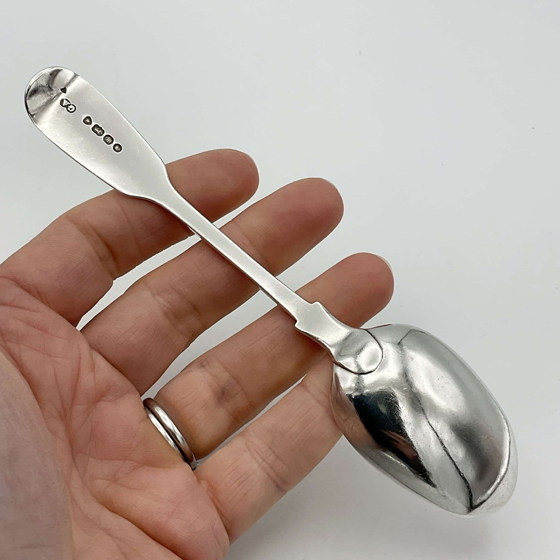 Antique silver teaspoon held upside down in a hand