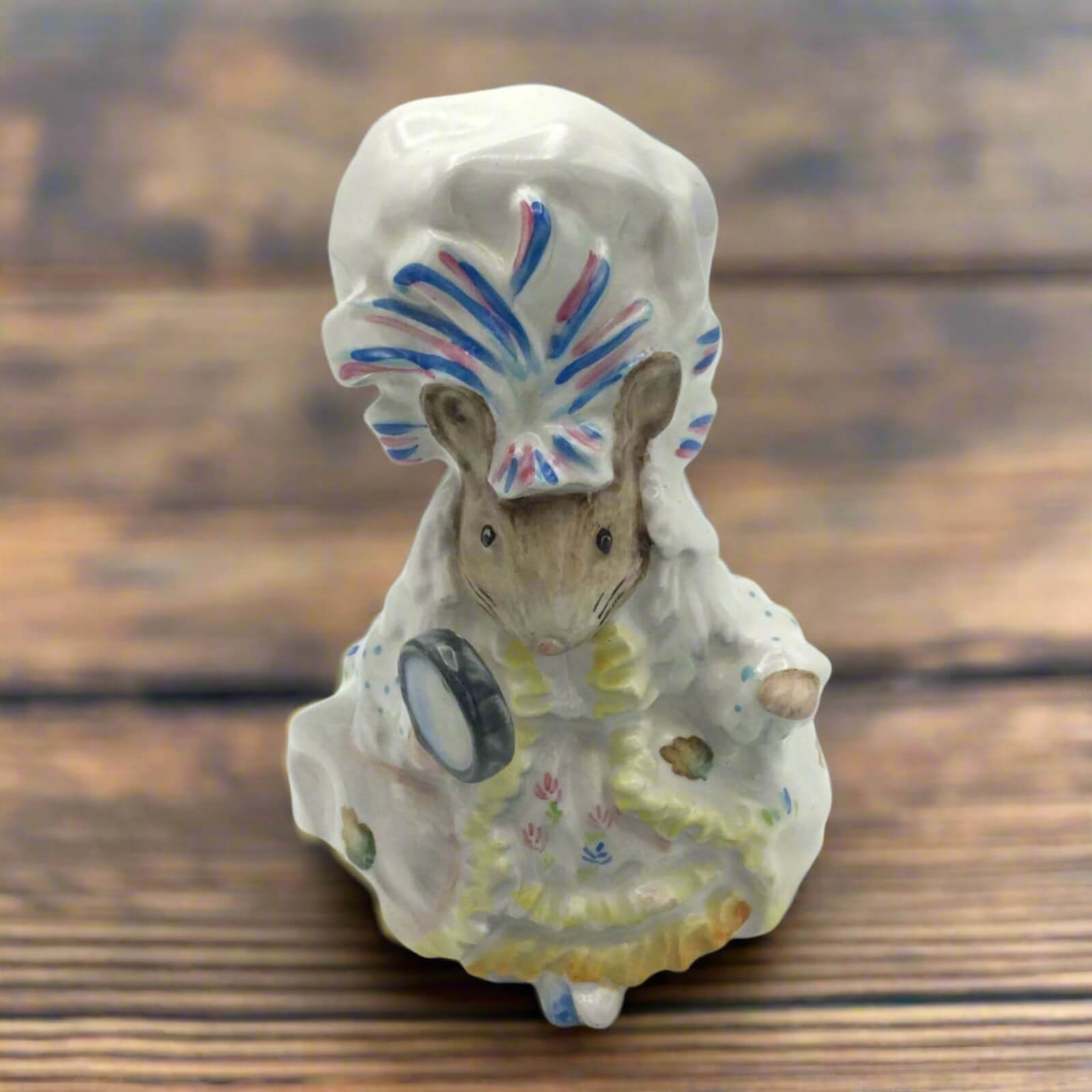 Small ceramic figure of a mouse with a colorful hat on a wooden surface