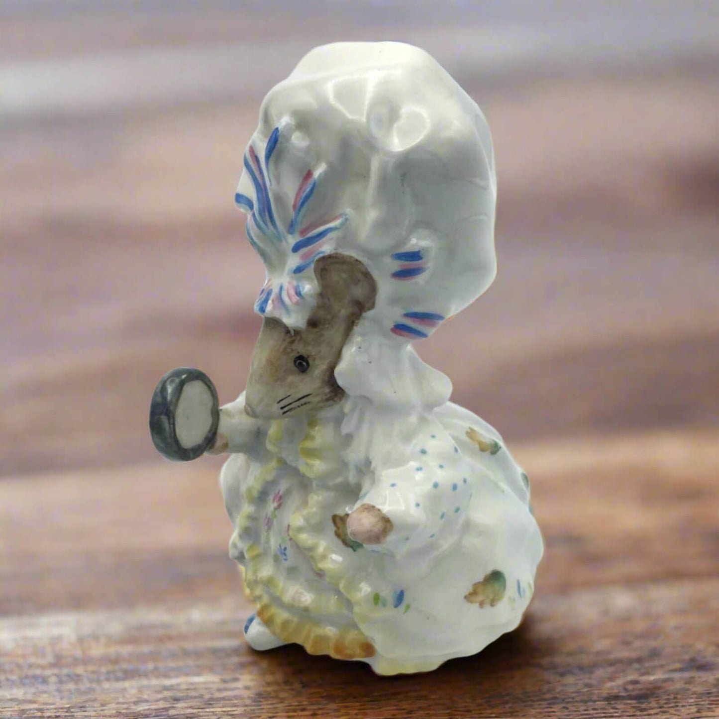 Small ceramic figurine of a mouse in a dress with a hat on a wooden surface