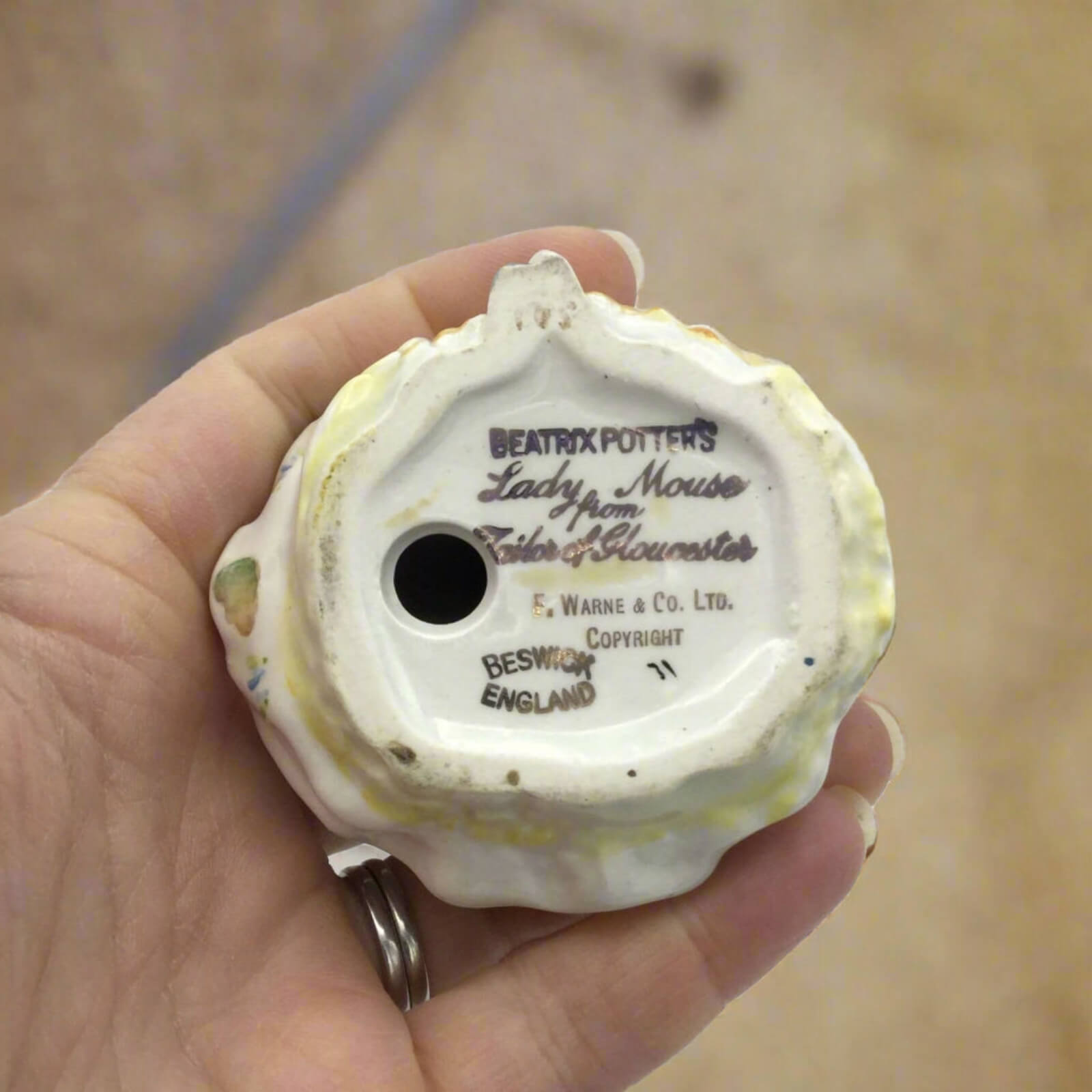 Small ceramic figure of a mouse with 'Beatrix Potter' branding held in a hand.