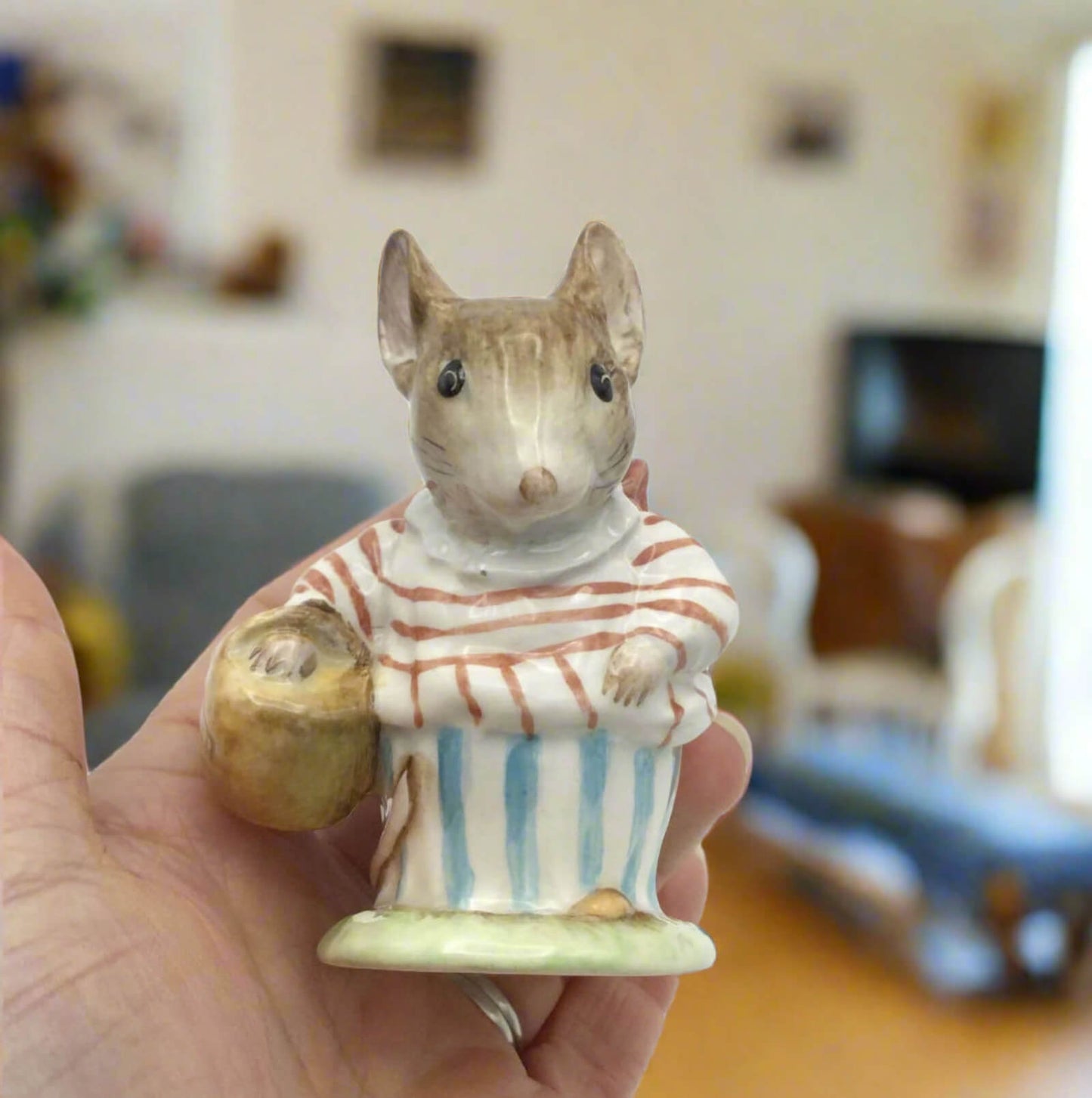 Small ceramic mouse figurine with a striped shirt held in a hand, blurred indoor background