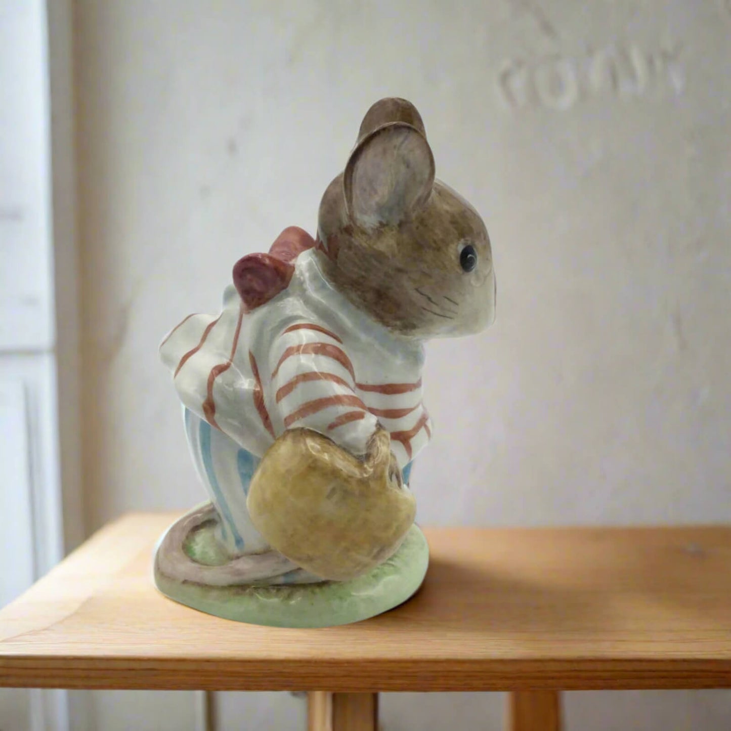 Small figurine of a mouse in a striped outfit on a wooden surface with a neutral background