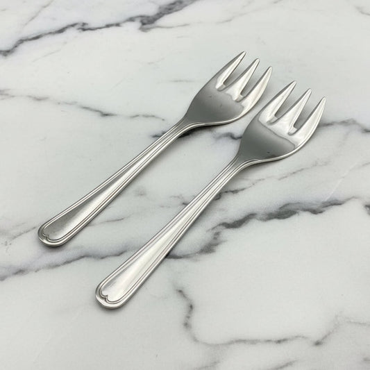 Two silver dessert forks on a marble surface