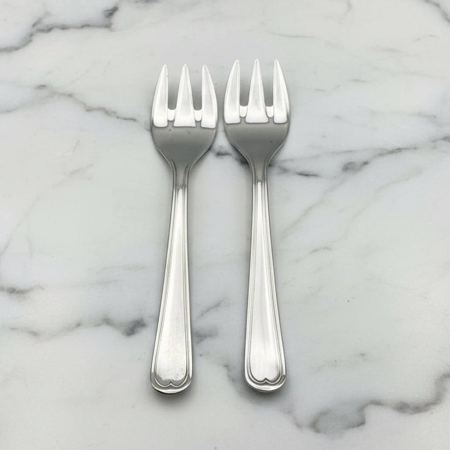Two silver forks on a marble surface
