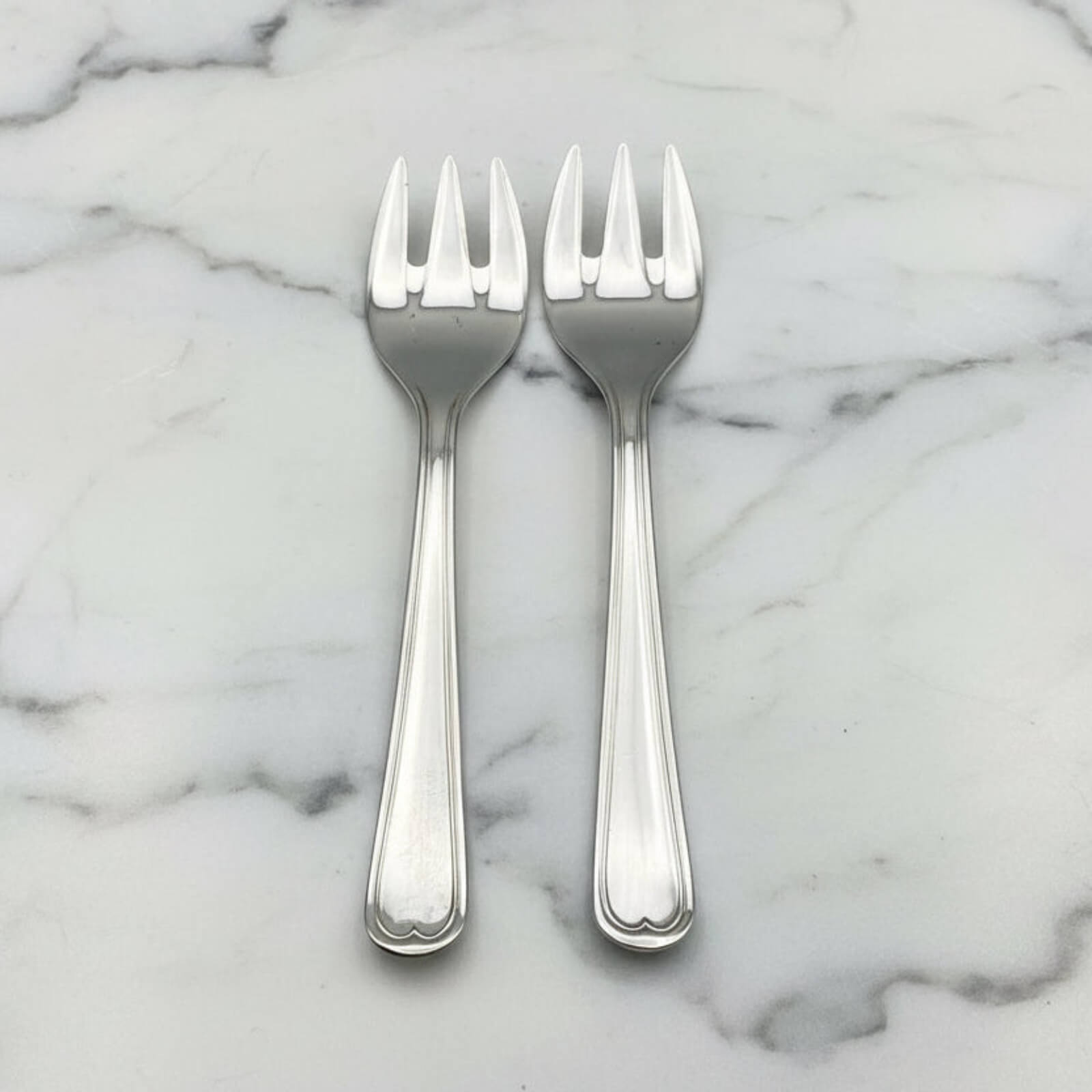 Two silver forks on a marble surface