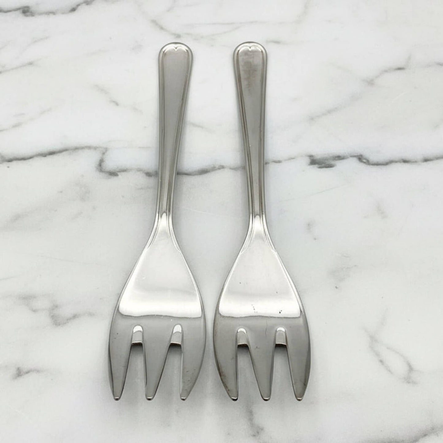 Two silver forks on a marble surface