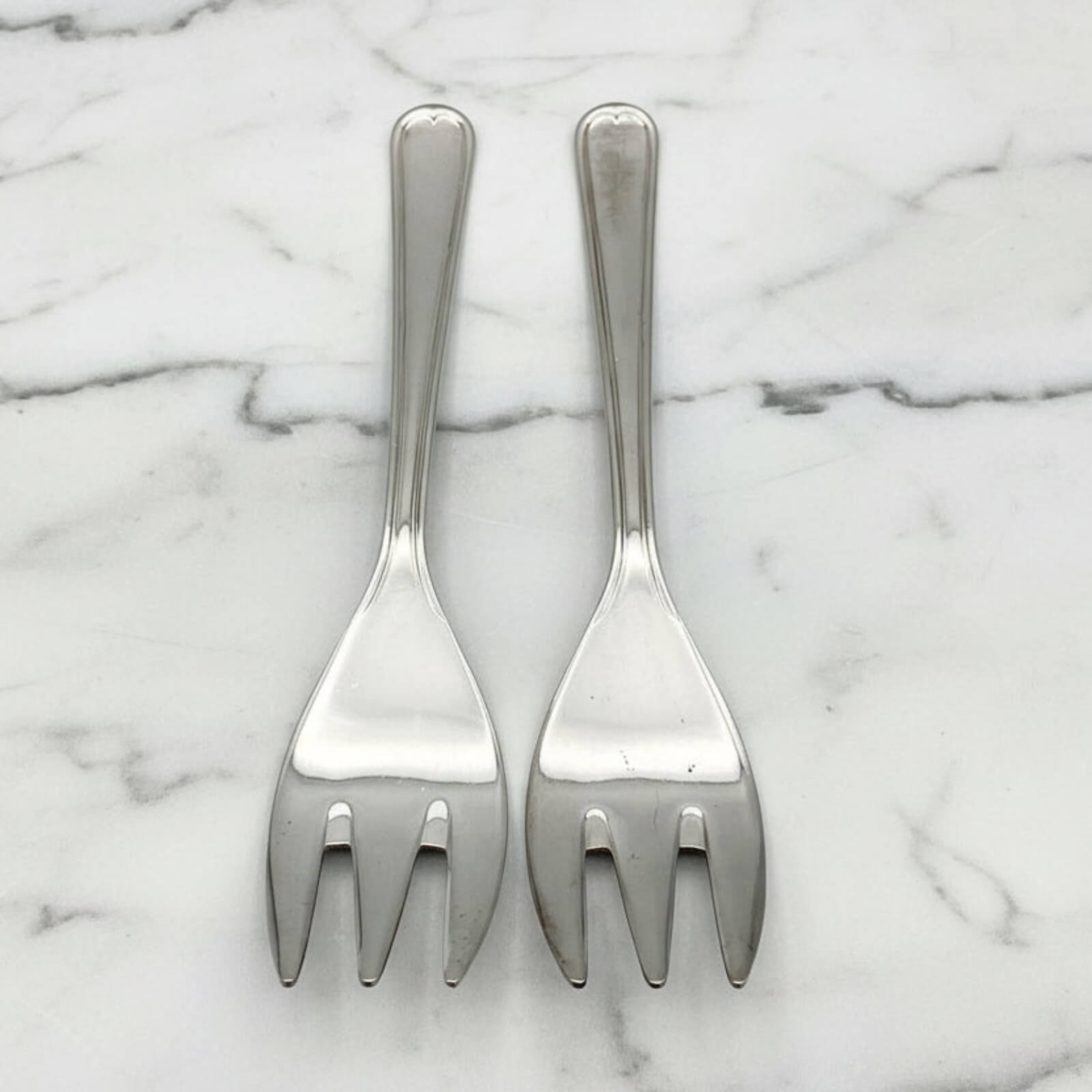Two silver forks on a marble surface