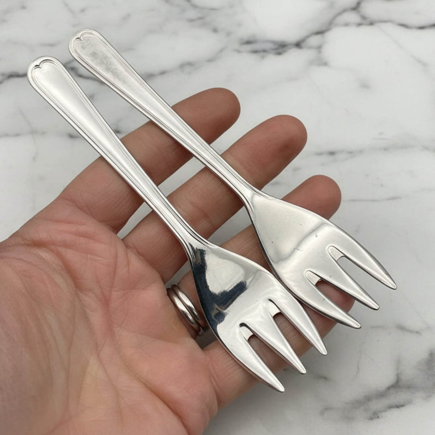 Two silver forks held by a hand on a marble background