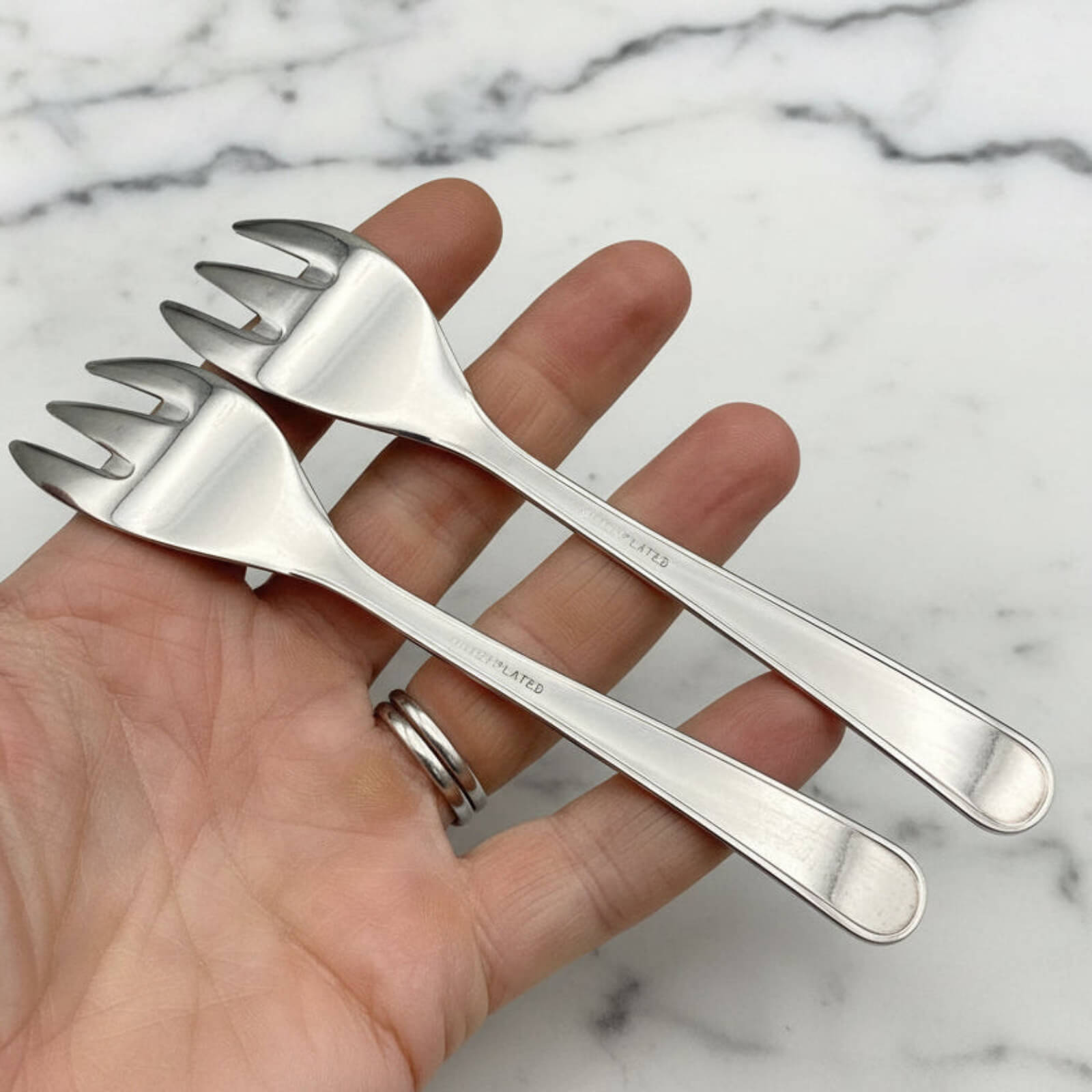 Set of silver forks held in a hand against a marble background