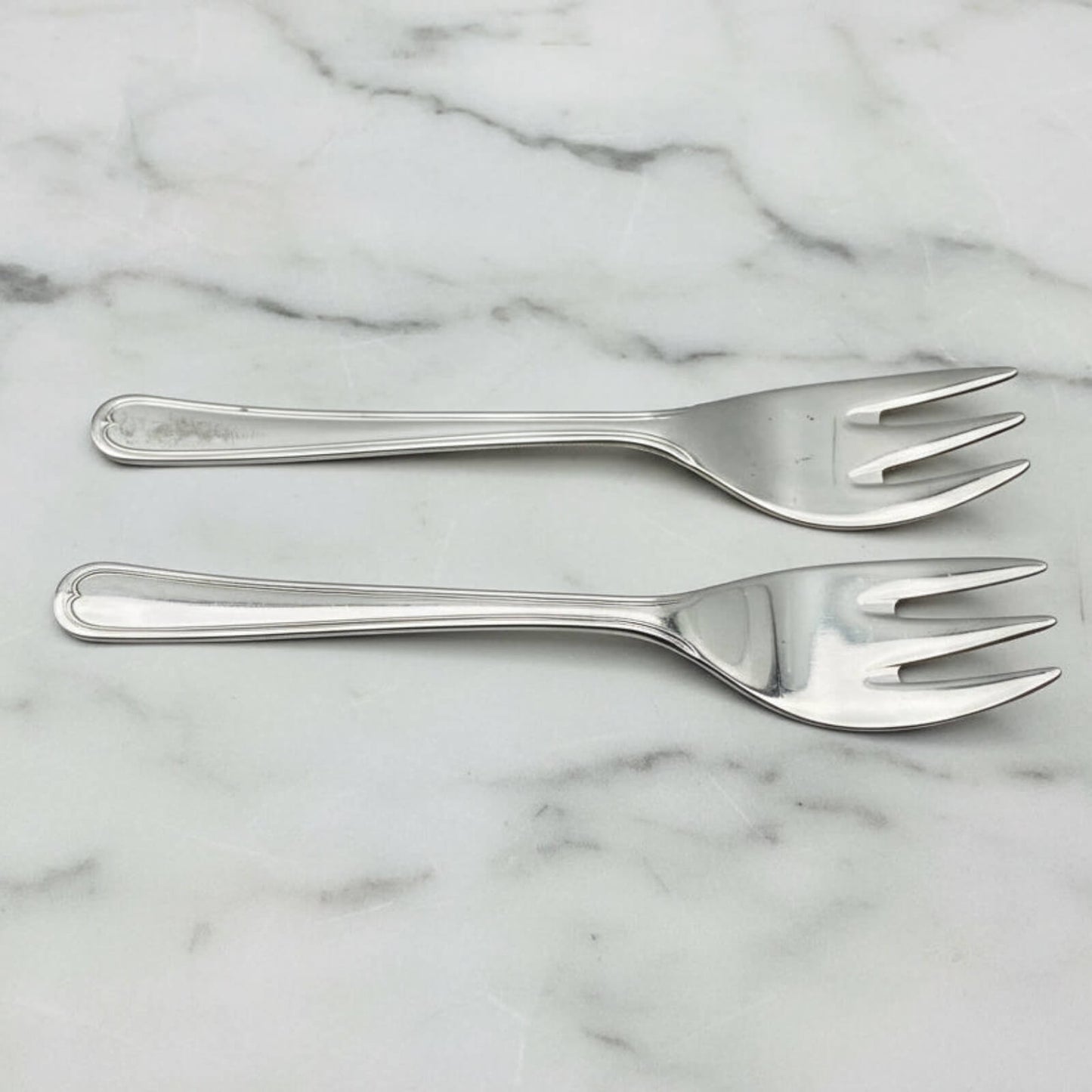 Two silver forks on a marble surface