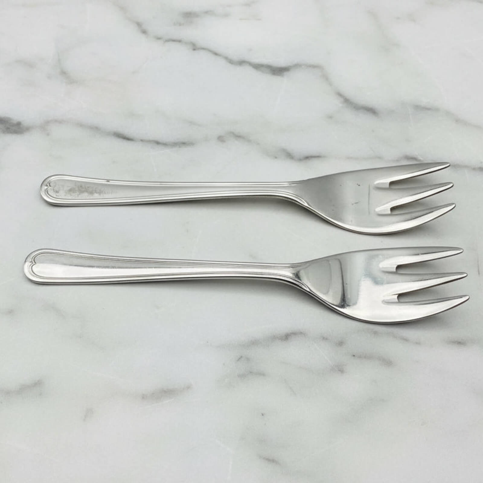 Two silver forks on a marble surface