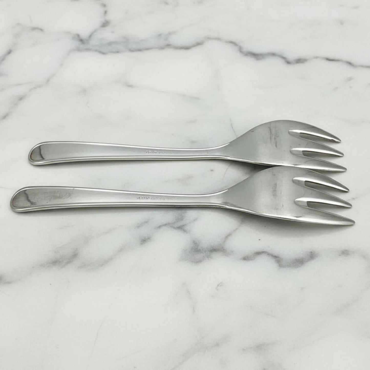 Two silver forks on a marble surface