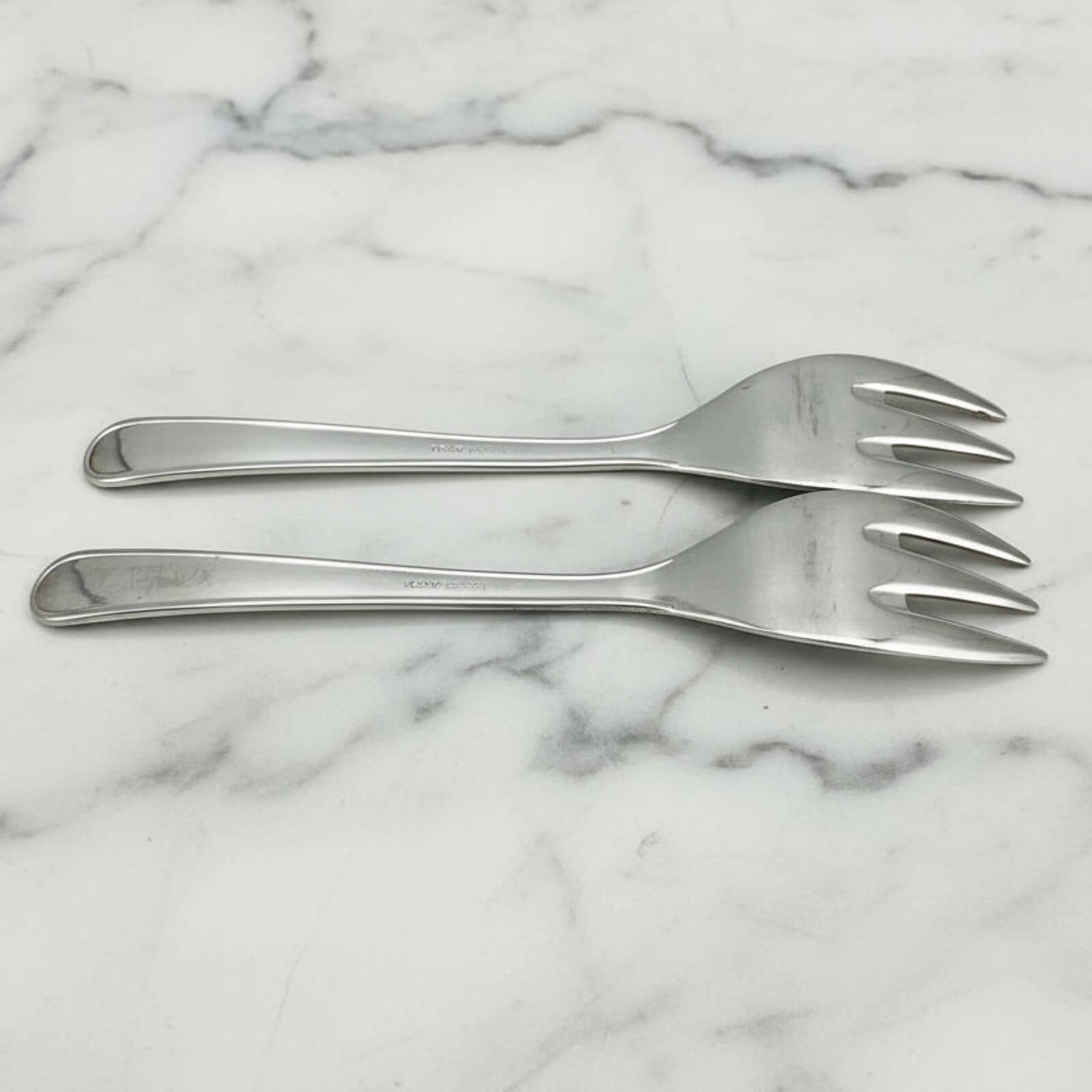 Two silver forks on a marble surface