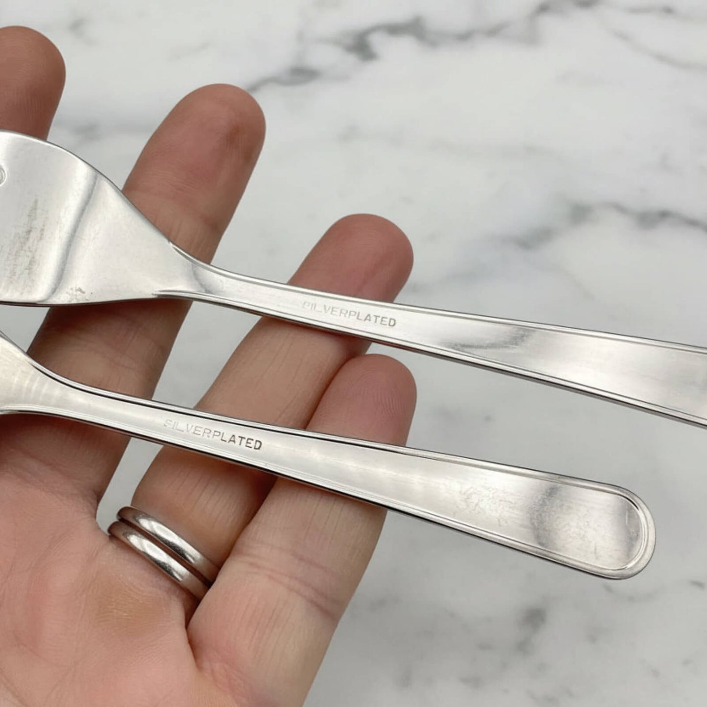 Two silver forks held in a hand with a marble background