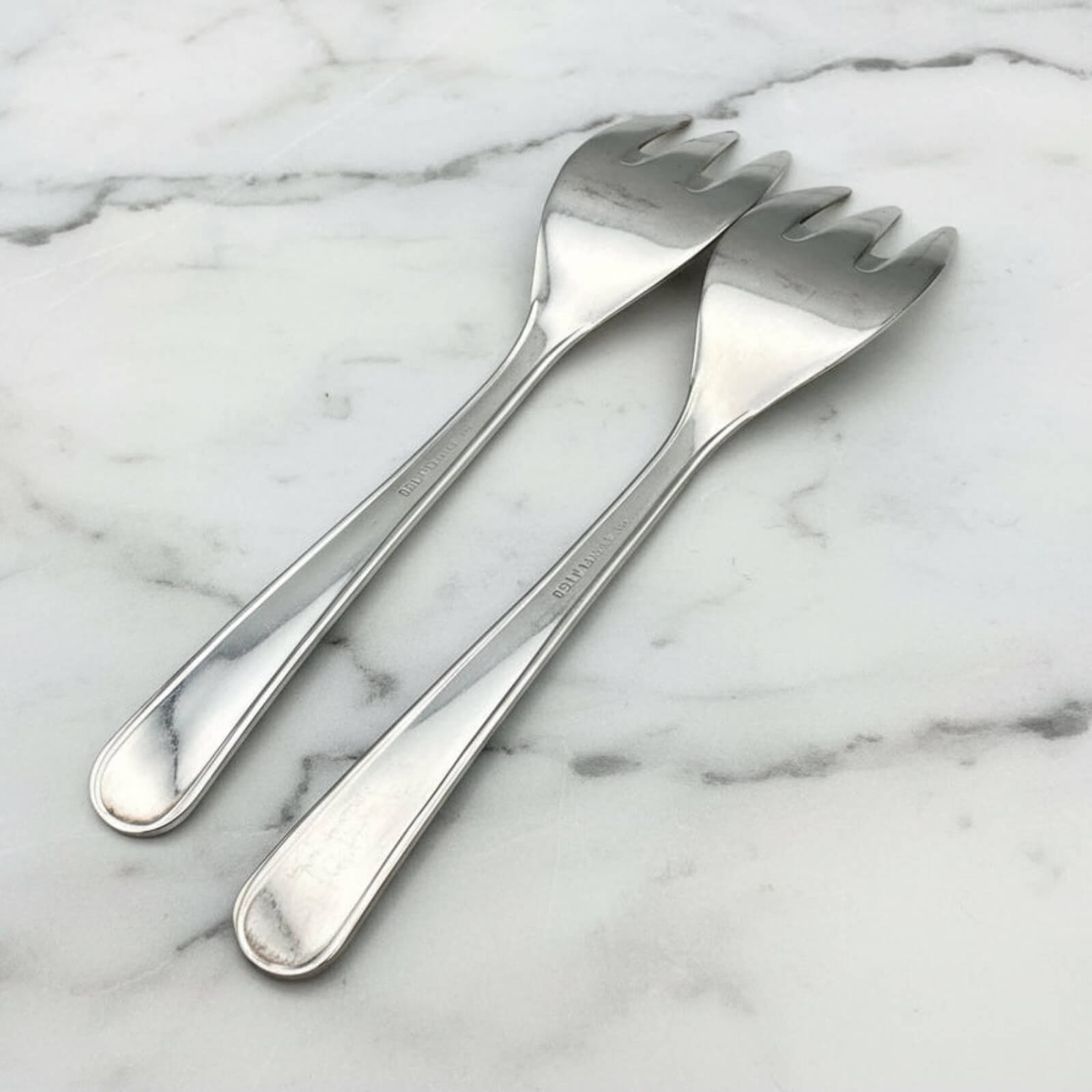 Two silver forks on a marble surface