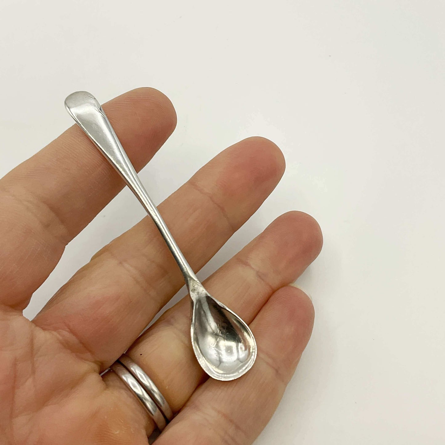 Small silver spoon held in a hand against a white background