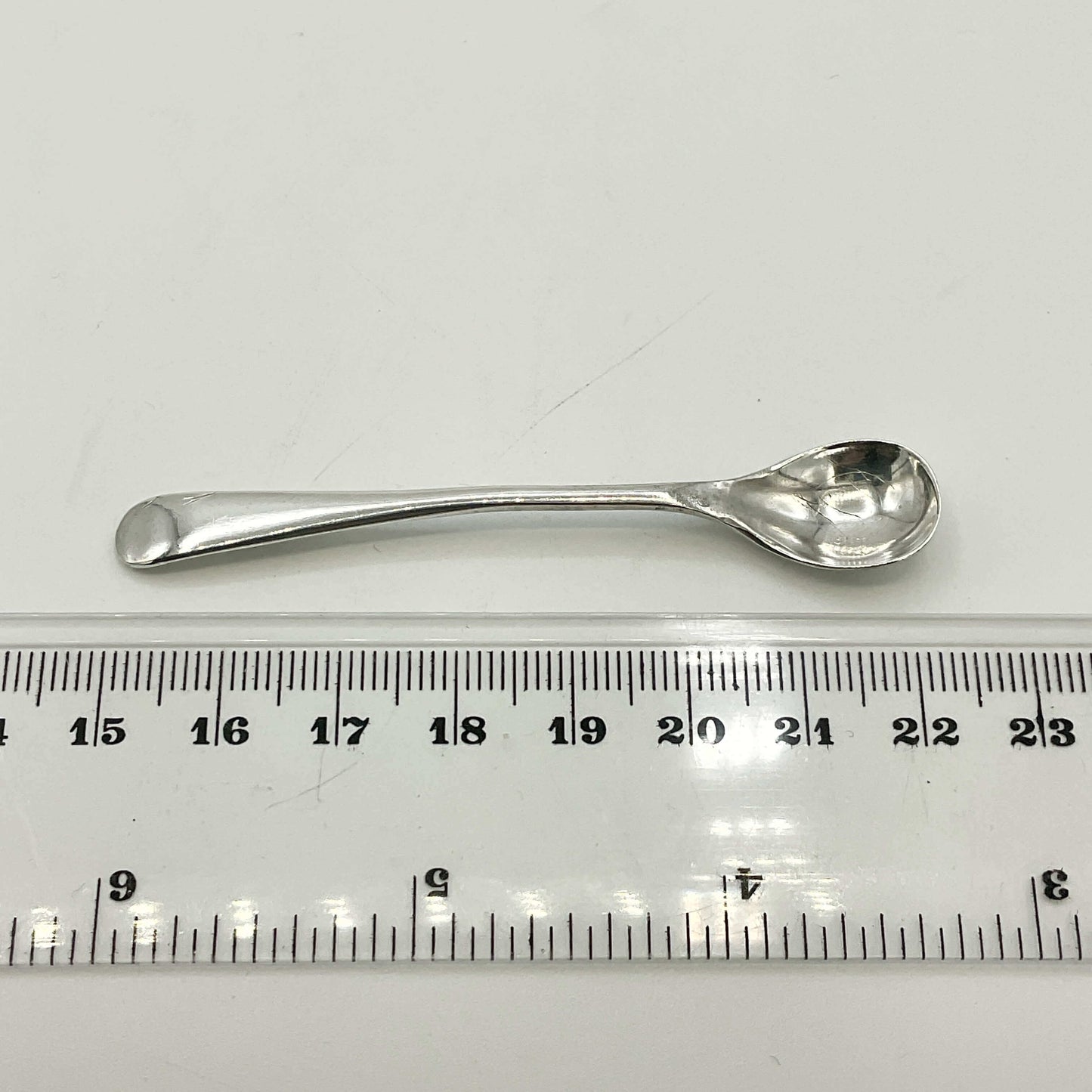 Silver spoon next to a ruler on a white background