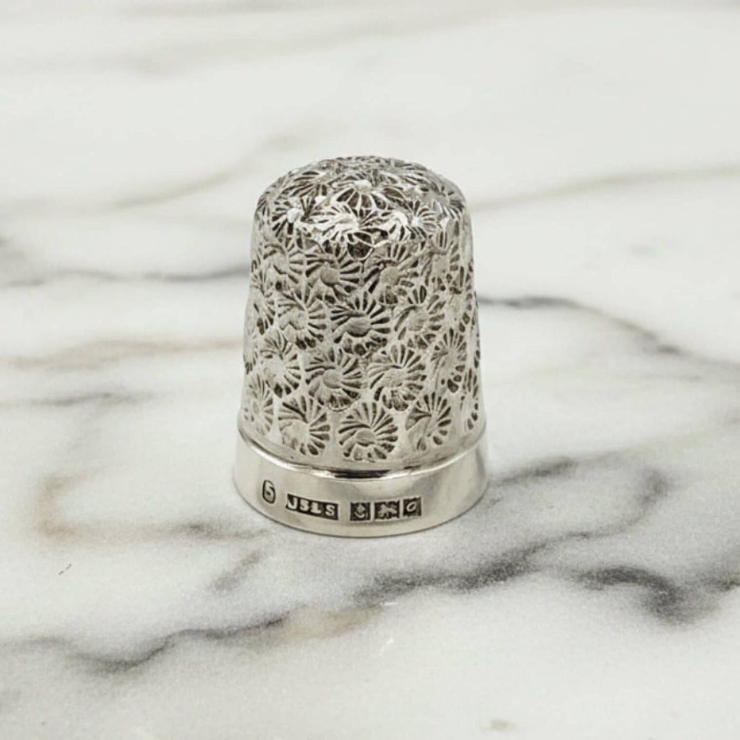 Silver thimble with intricate floral patterns on a marble surface