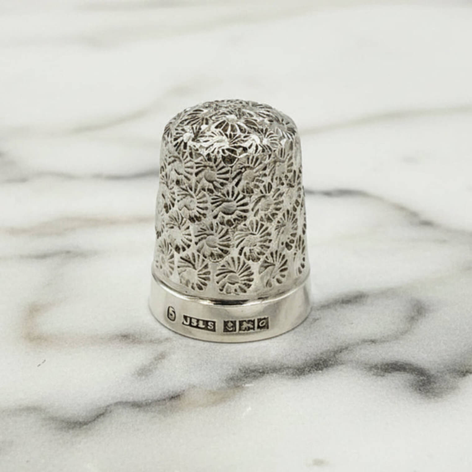 Silver thimble with intricate floral patterns on a marble surface