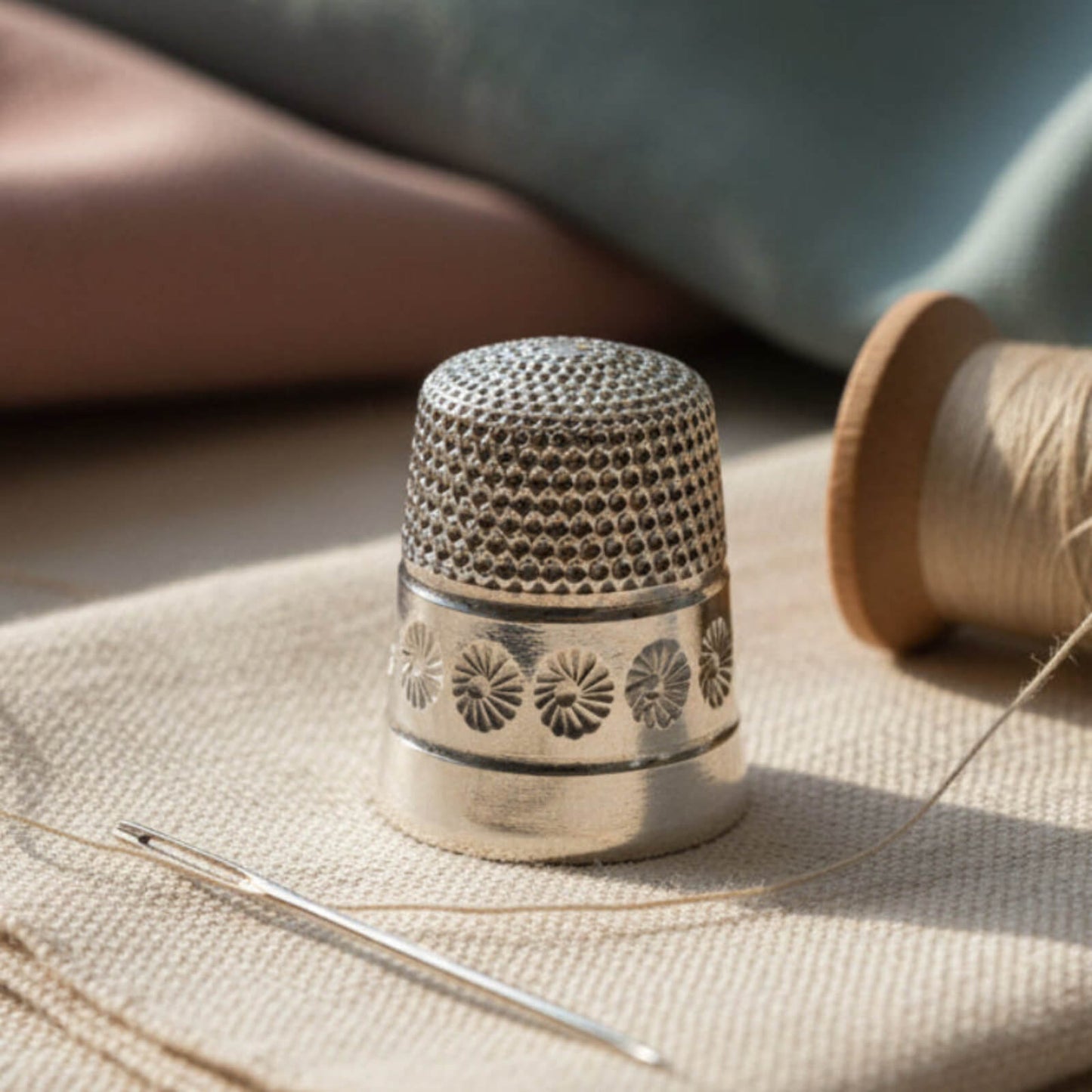 Silver thimble with sewing needle and thread on fabric background