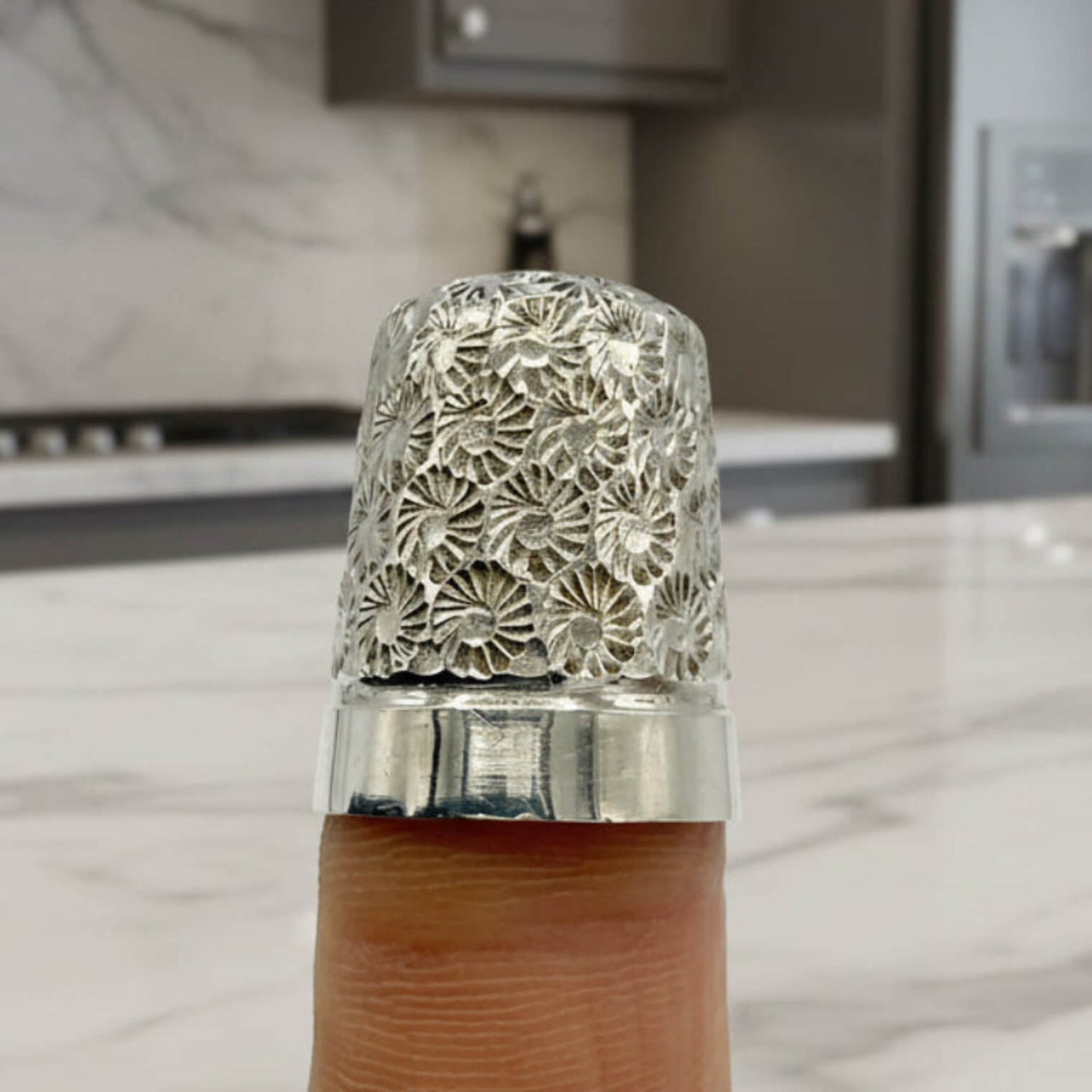 Decorative silver thimble on a finger with a blurred kitchen background