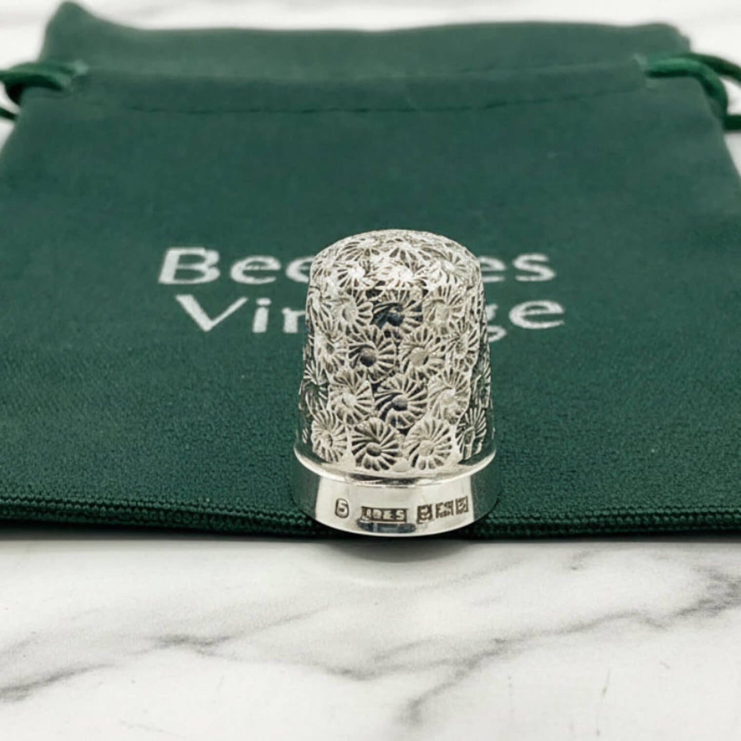 Silver thimble with intricate design on a green velvet bag with 'Beeches Vintage' text.