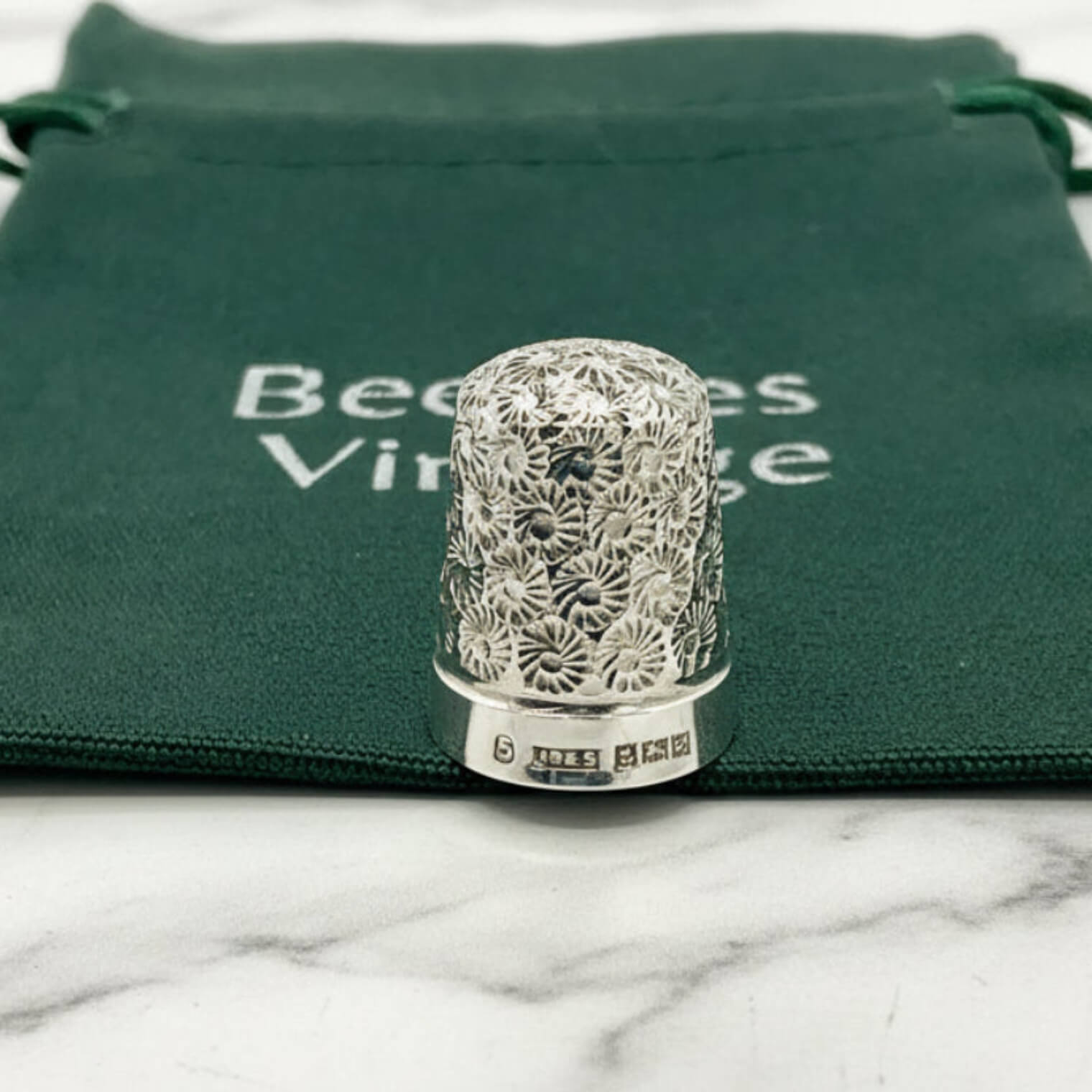Silver thimble with intricate design on a green velvet bag with 'Beeches Vintage' text.