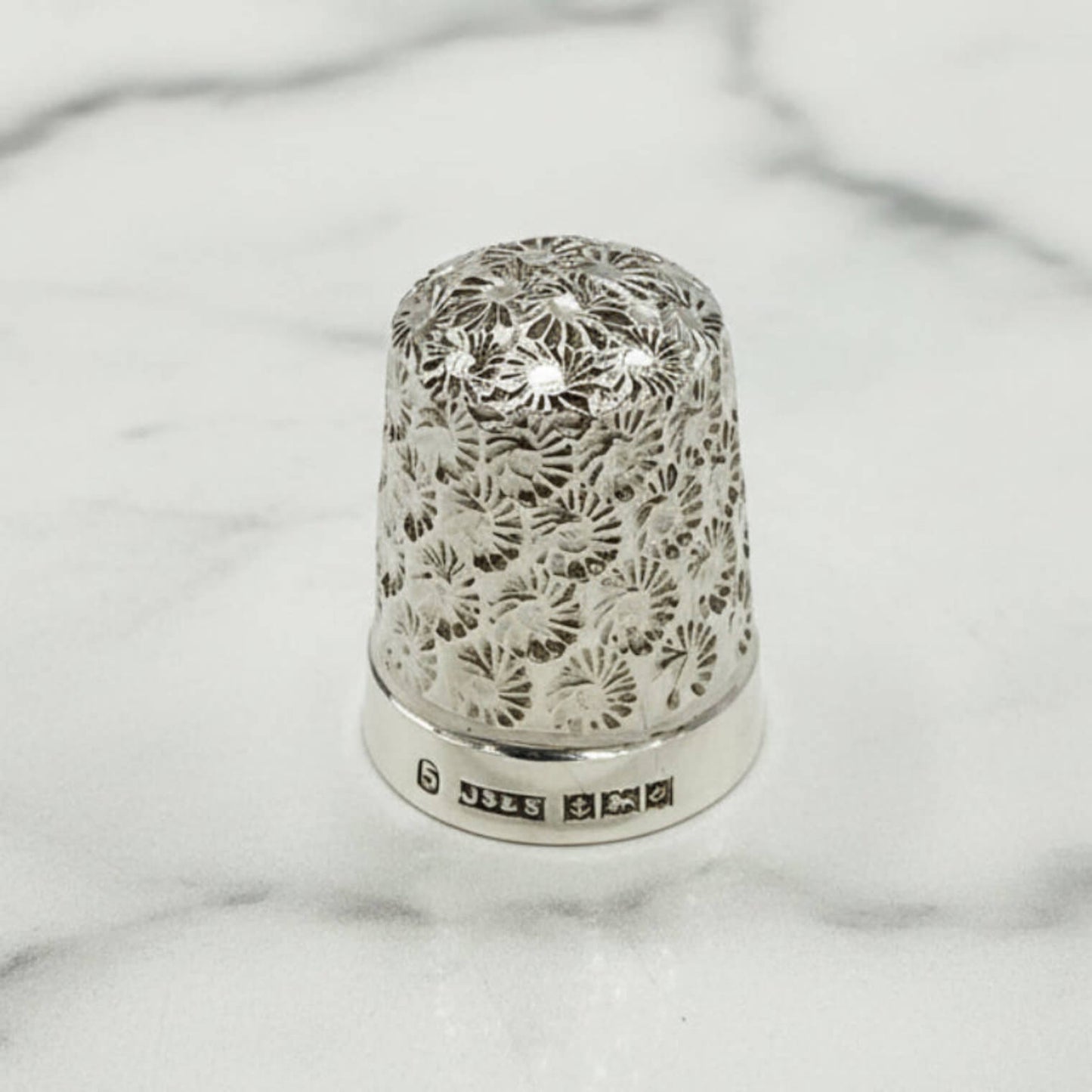 Silver thimble with intricate floral patterns on a marble surface