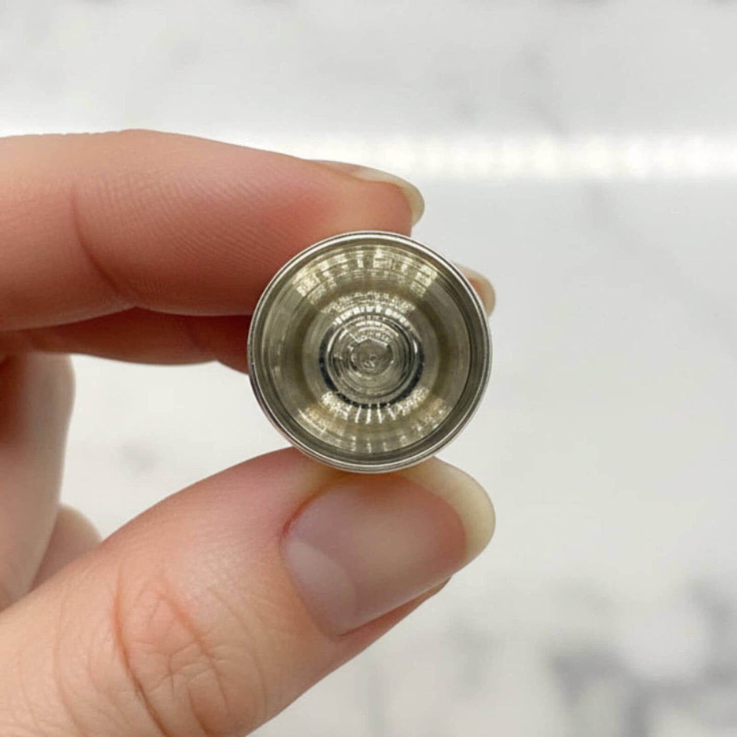 Hand holding a silver thimble against a neutral background