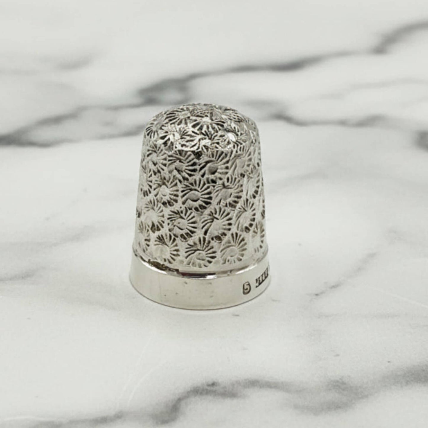 Silver thimble with intricate lace pattern on a marble surface