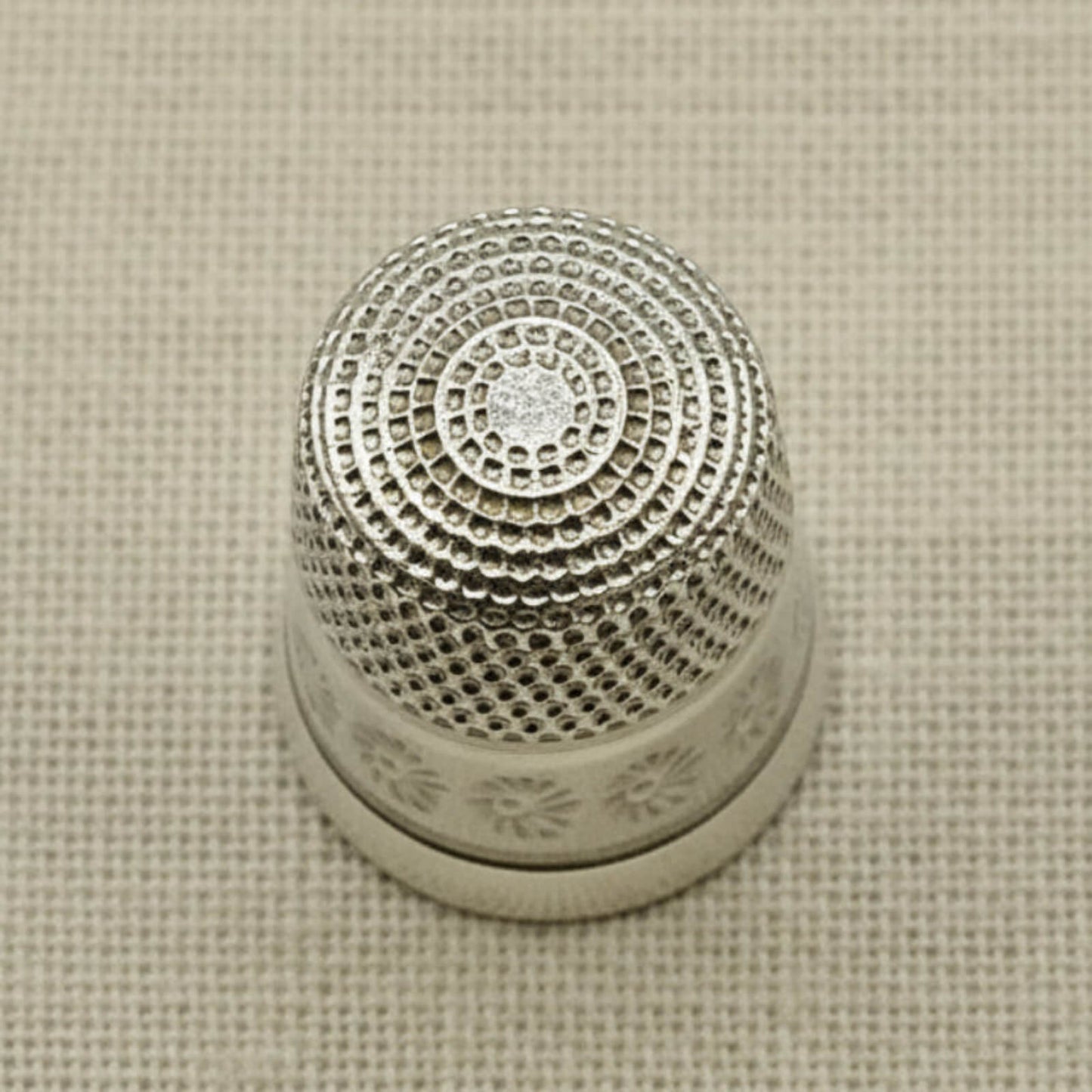 Silver thimble with intricate design on a beige fabric background