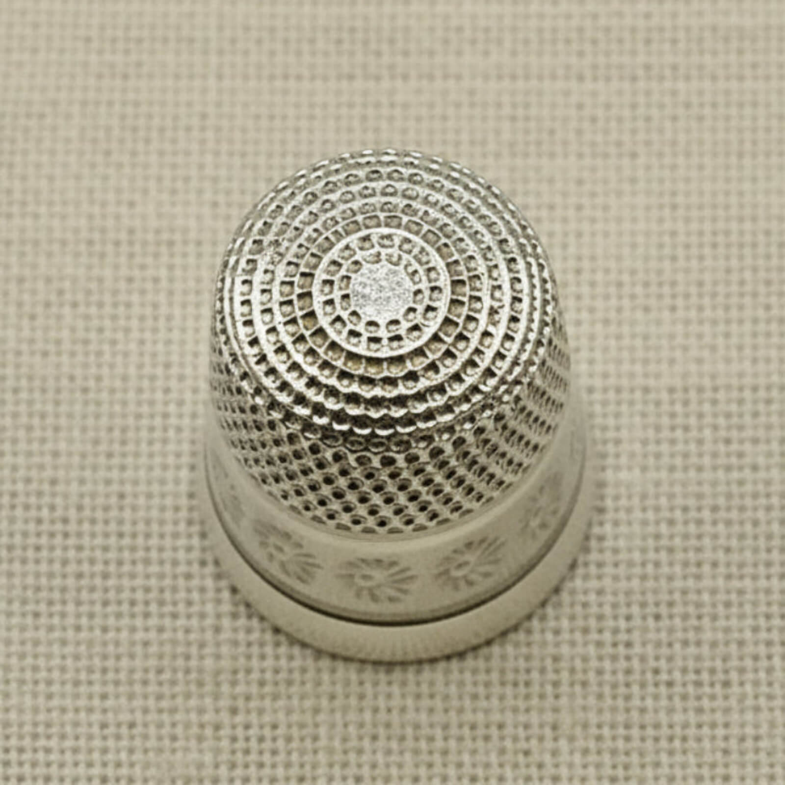 Silver thimble with intricate design on a beige fabric background