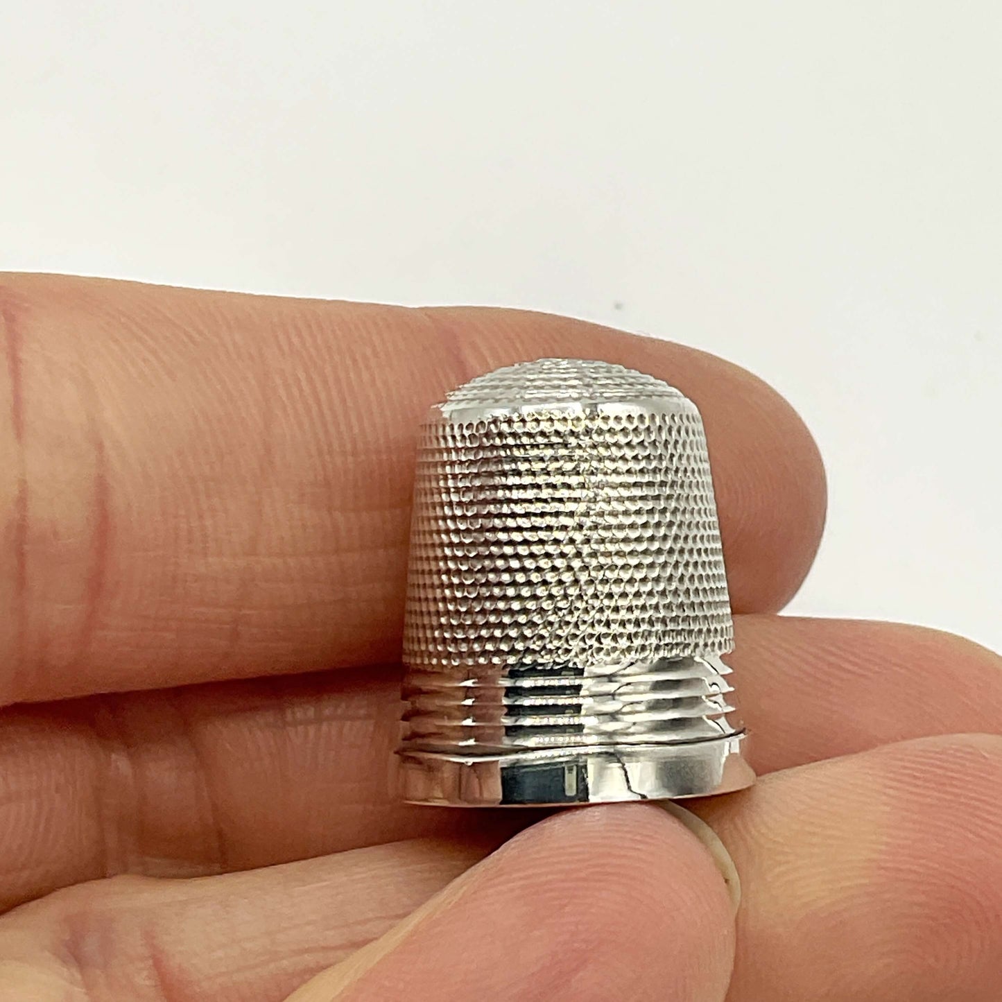 Silver thimble held between fingers against a white background