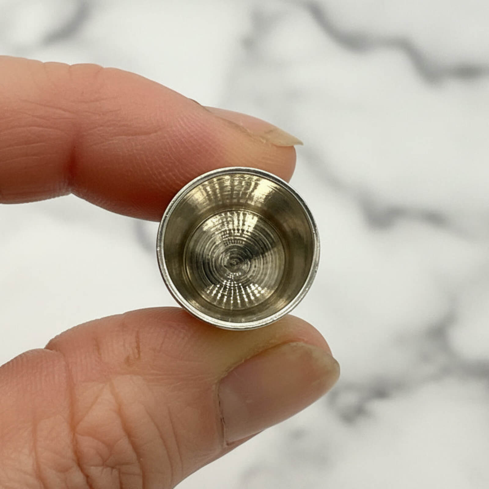 Gold-colored metal object held between fingers against a marble background