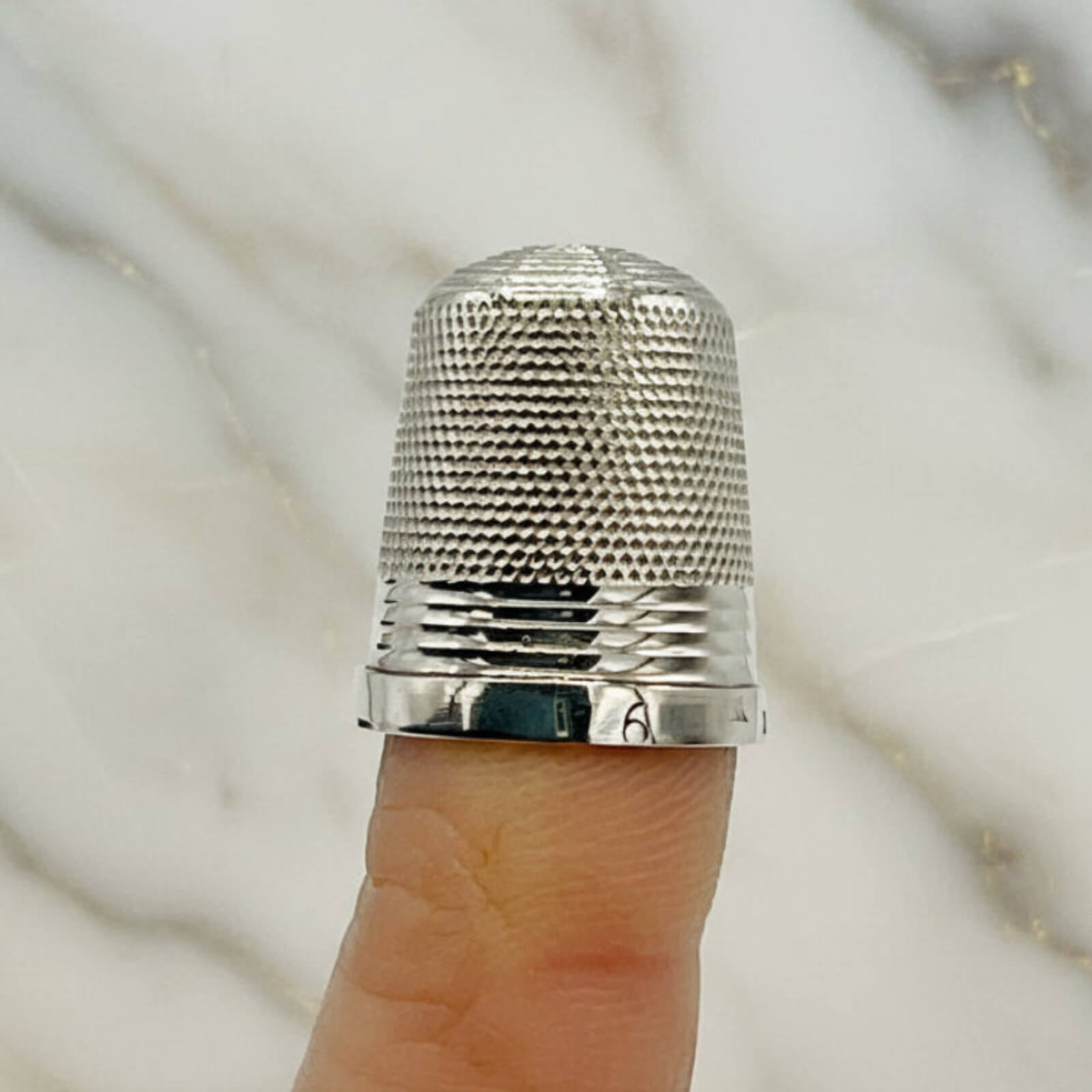 Silver thimble on a finger against a marble background