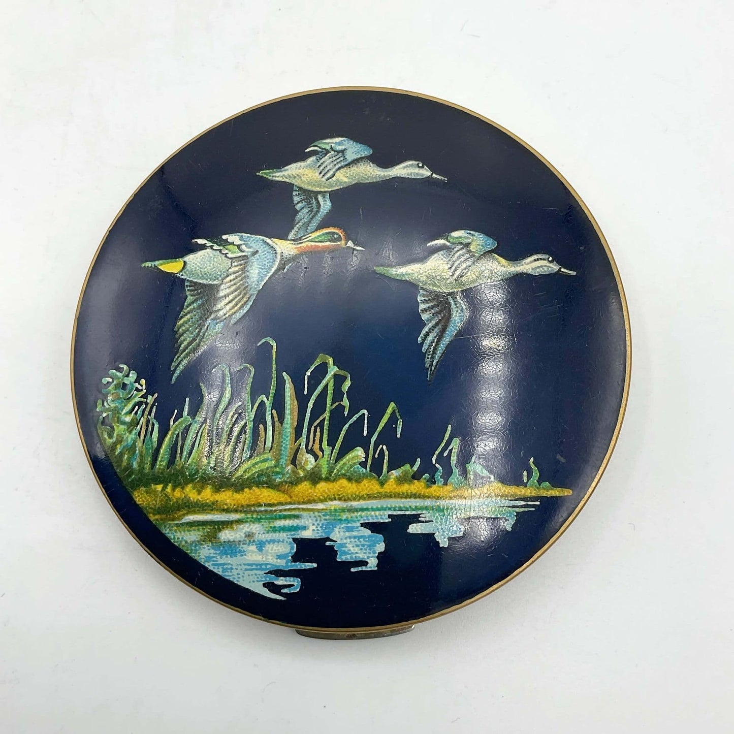 beautiful enamel featuring three ducks flying over water on a mirror compact lid and white background